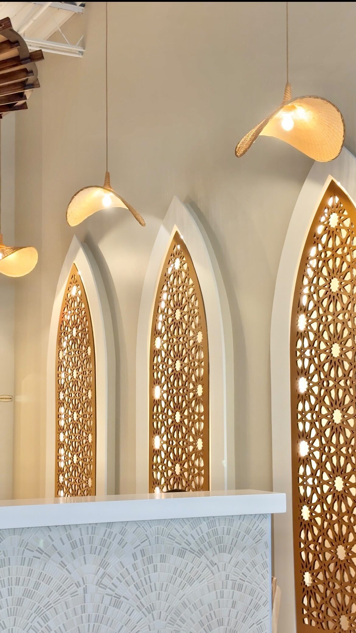 Three carved-lattice mihrab arches in cream stucco, backlit with golden light, inside an Arwa Yemeni Coffee cafe.